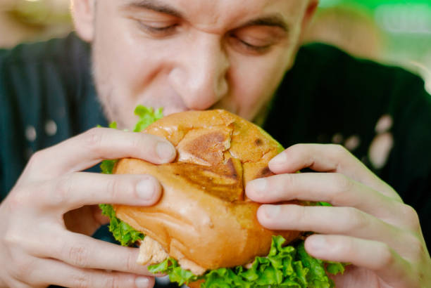 istock Man in a restaurant eating a hamburger, he is hungry and having a good bite. selective focus 1153409543