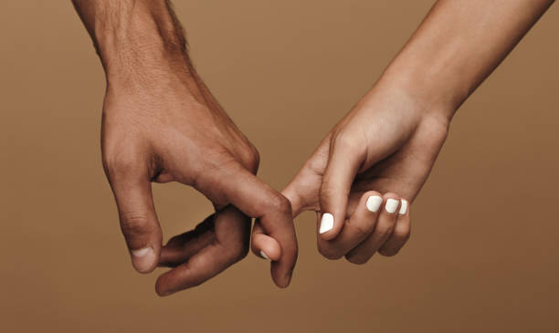 Couple linking index fingers Close up of a couple linking index fingers. Man and woman in love linking index fingers against brown background couple holding hands stock pictures, royalty-free photos & images