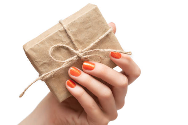 istock Female hand with orange nail design holding gift box 1153416976