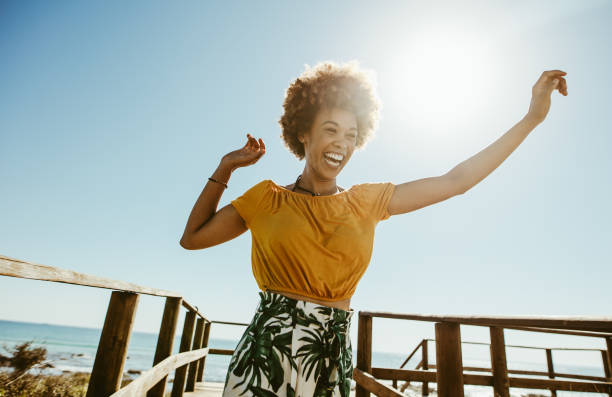 Woman having fun on summer vacation Excited young woman running on a boardwalk with her hands raised on a sunny day. African female having fun on summer vacation at the seaside. outdoor living stock pictures, royalty-free photos & images