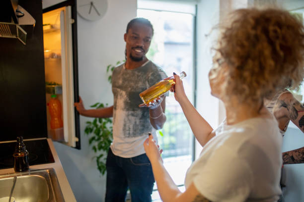 Young man opening fridge and passing the beer to his flatmate Young African-American opening fridge and passing a bottle of root beer to his female flatmate flatmate stock pictures, royalty-free photos & images