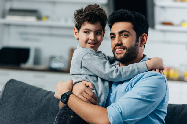 istock cheerful latin father hugging cute son at home 1153423847