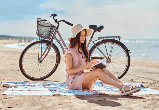 istock Young woman holds a book and looking at camera while sitting on the beach. 1153424474