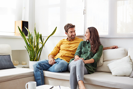 Shot of a smiling young couple talking together while relaxing in their living room