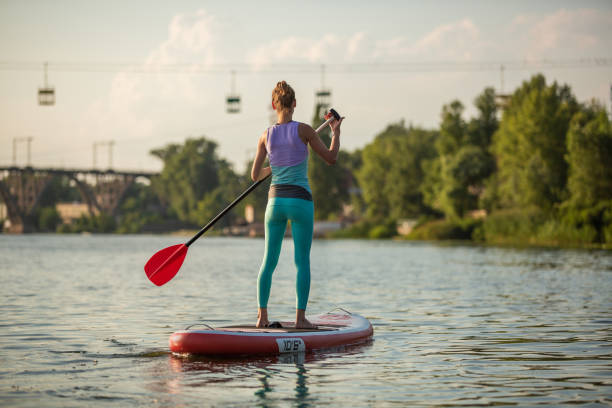 mujer atlética joven haciendo fitness en una tabla con un remo en un lago. - paddleboard oar women lake fotografías e imágenes de stock