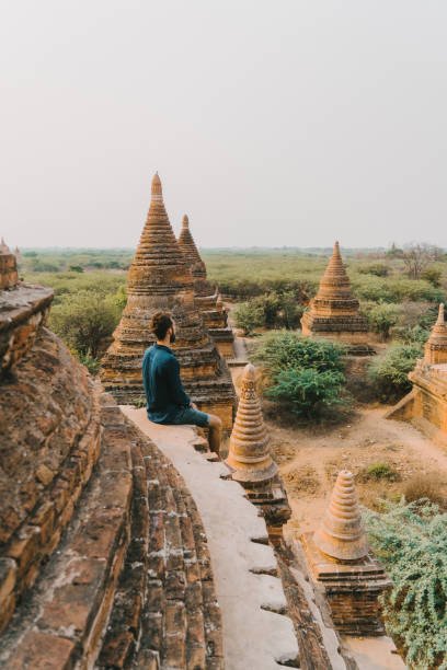 Man looking at scenic  view of Bagan Heritage Site from above Young Caucasian man sitting and  looking at scenic  view of Bagan Heritage Site from above bagan archaeological zone stock pictures, royalty-free photos & images