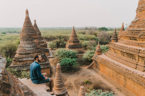 Man looking at scenic  view of Bagan Heritage Site from above Young Caucasian man sitting and  looking at scenic  view of Bagan Heritage Site from above bagan archaeological zone stock pictures, royalty-free photos & images
