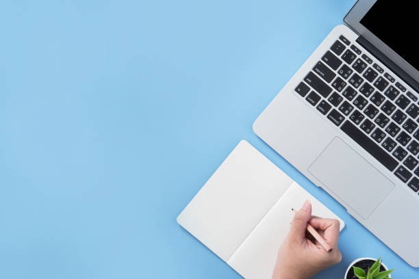 istock Girl write on open white book or accounting on a minimal clean light blue desk with laptop and accessories, copy space, flat lay, top view, mock up 1153432521