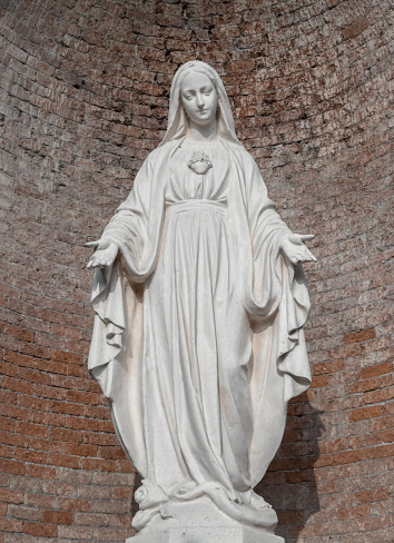 Statue in stone of Virgin Mary. On background, red brick wall. Ideal for christmas and easter concepts and other.