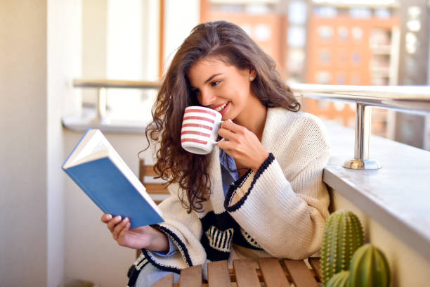istock Young woman reads a book and drinks tea at balcony 1153435158