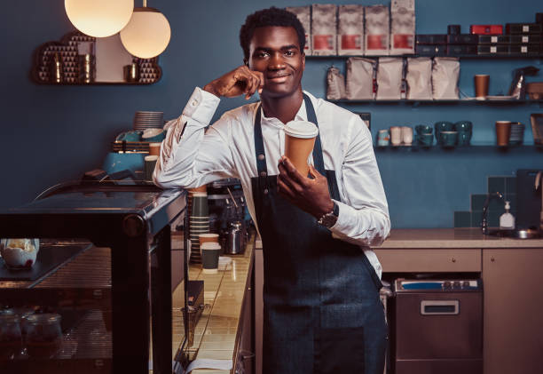istock African barista smiling at camera relaxing after workday with coffee while leaning on the counter at coffee shop. 1153439981