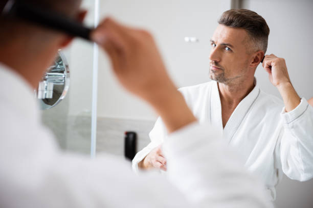 istock Man in white bathrobe looking at the mirror and combing his hair 1153440552