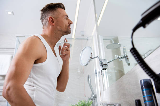 istock Smiling man standing in front of the mirror and spraying perfume 1153440645