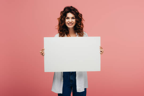 istock happy young woman holding blank placard while standing on pink 1153441508
