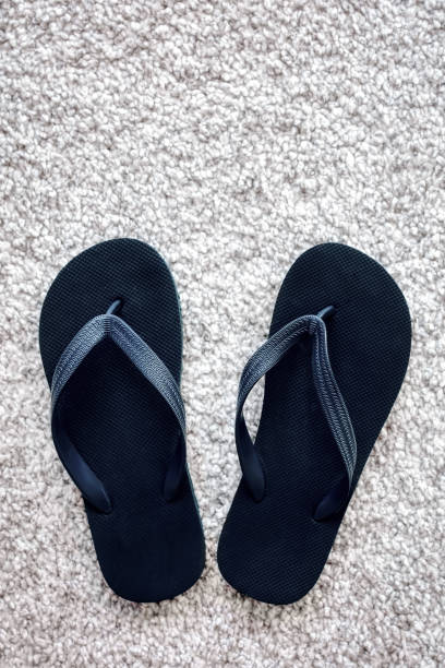 istock Pair of black rubber flip flops on white carpet 1153441545
