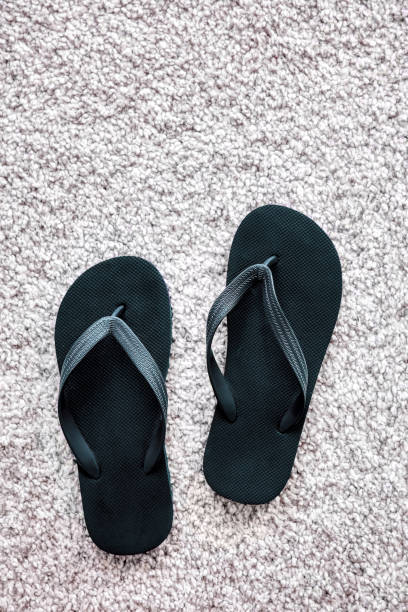 istock Pair of black rubber flip flops on white carpet 1153441806