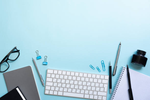 istock Office table desk with laptop, notebook, glasses, keyboard, pencil on blue background  with copy space 1153445210