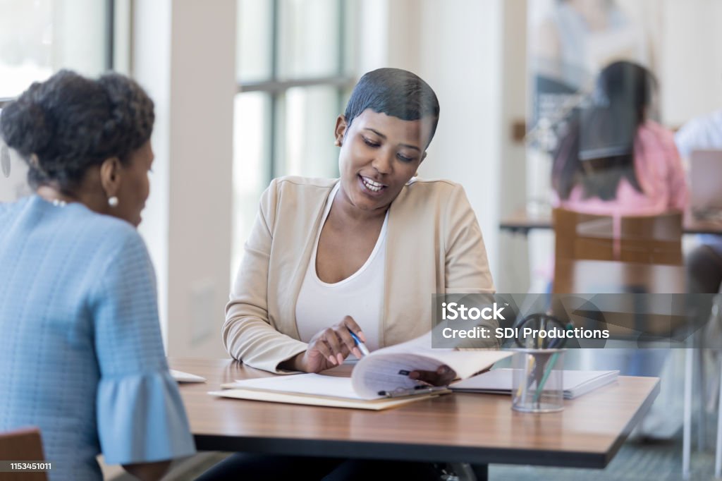 Mid adult loan officer with customer Mid adult African American female loan officer reviews loan terms with a female customer. Credit Union Stock Photo