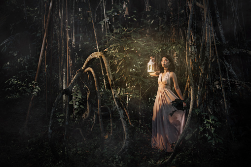 an asian chinese female at the jungle at night holding a lamp looking away