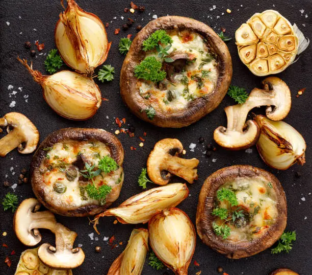 Photo of Roasted portobello mushrooms stuffed with cheese and herbs on a black iron  background, top view.