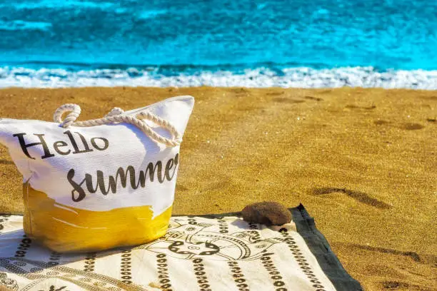 Photo of image of a beach bag on top of a towel overlooking the sea and sunbeams on which to put hello summer.