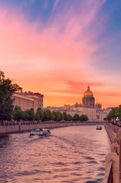 Summer sunset landscape of Saint Petersburg, Russia. Saint Isaac Cathedral across Moyka river. Pleasure boats on the quay of the Moyka embankment and buildings of architectural style classicism, city of Saint Petersburg