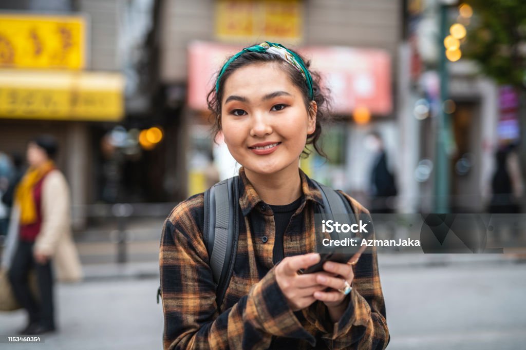 Young Mongolian Female Traveler Texting in Tokyo Self-sufficient young Mongolian vacationer searching her smart phone for ideas of how to spend the evening in Tokyo. Mongolian Ethnicity Stock Photo