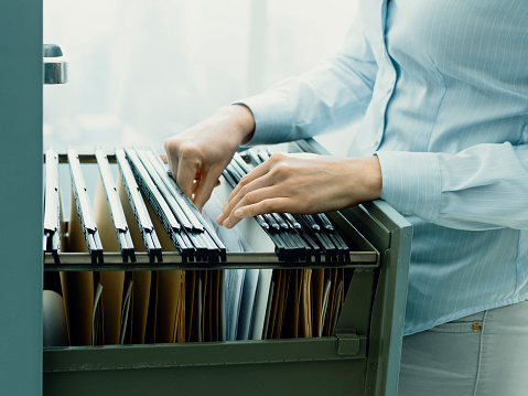 Professional female office clerk searching files and paperwork in the filing cabinet