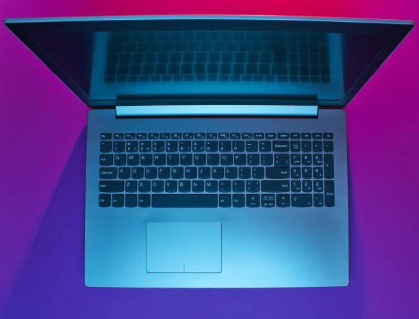 istock Modern laptop with vibrant gradient pink blue neon  lights. Minimalism. Top view 1153463340