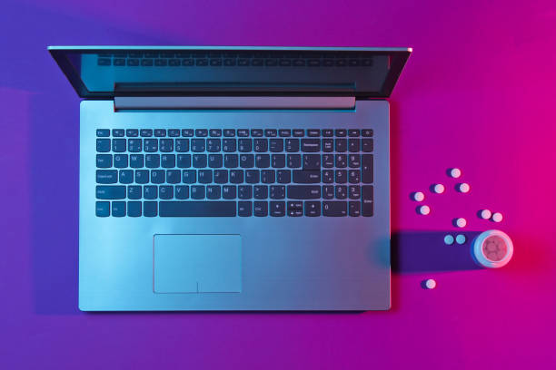 istock Internet addiction concept. Modern laptop, bottle pills with vibrant gradient pink blue neon  lights. Minimalism. Top view 1153463395