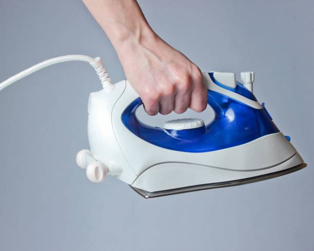 istock Female hand holding iron for ironing against gray background. 1153464400
