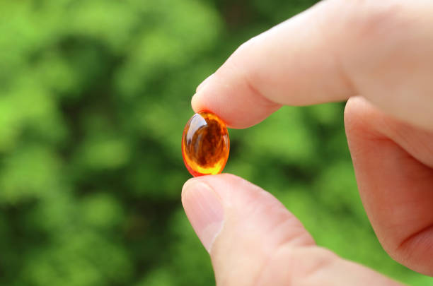 目がかすんだ緑の葉に対して透明なサプリメント gelcap を保持するクローズアップ男の指 - vitamin pill red pill capsule ストックフォトと画像