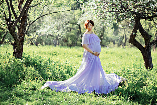 Pregnant woman in fluttering purple dress in park