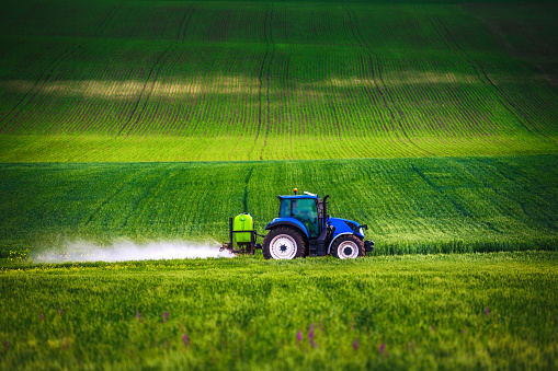 Farming tractor plowing and spraying on field.