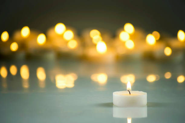 A lit white candle on a background of blurred yellow lights