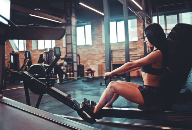 istock Purposeful fit brunette in sportswear sitting on the simulation rowing exercise machine 1153471486