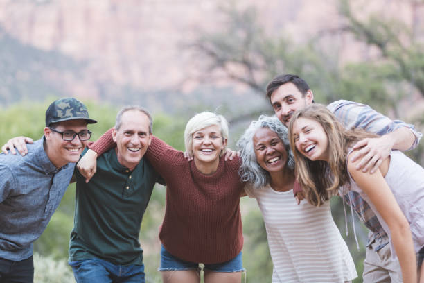 Multi-generational of friends posing together outside A multiethnic group of friends embrace and smile at the camera. They're lined up loosely and desert vegetation and sagebrush are in the background. adult age stock pictures, royalty-free photos & images