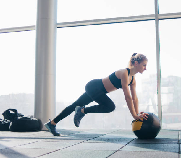 Athletic attractive woman doing exercise lifting the leg up leaning on the medicine ball against the background of large panoramic window in the gym. Functional training Athletic attractive woman doing exercise lifting the leg up leaning on the medicine ball against the background of large panoramic window in the gym. Functional training chest dip on athletic workout stock pictures, royalty-free photos & images