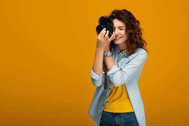 istock happy redhead photographer taking photo while holding digital camera on orange 1153476176