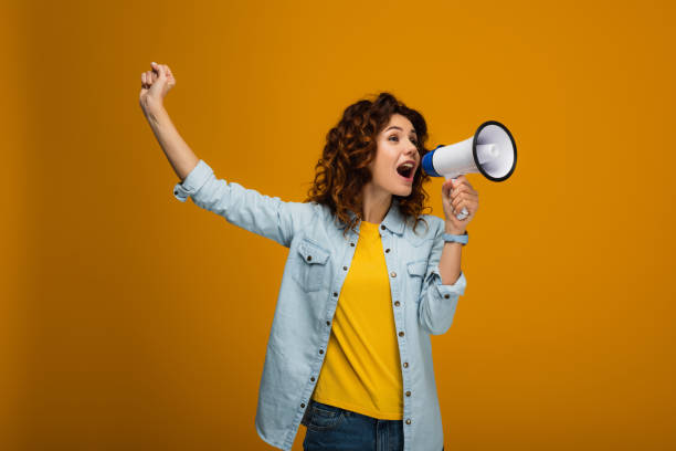 istock curly redhead woman screaming in megaphone and gesturing on orange 1153476199