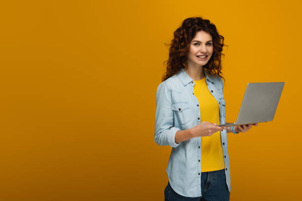istock beautiful and cheerful redhead girl using laptop on orange 1153476409