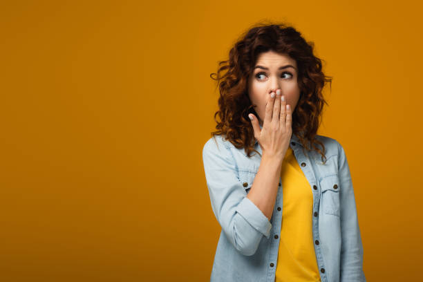 istock surprised redhead woman covering mouth while standing on orange 1153477659