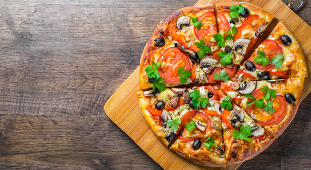 istock sliced Pizza with Mozzarella cheese, Tomatoes, pepper, olive, mushrooms, Spices and Fresh leaf. Italian pizza on wooden table background 1153485700