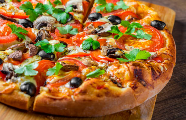 istock sliced Pizza with Mozzarella cheese, Tomatoes, pepper, olive, mushrooms, Spices and Fresh leaf. Italian pizza on wooden table background 1153485710
