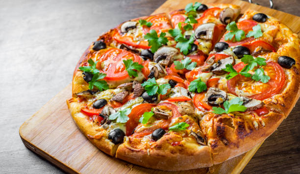 istock sliced Pizza with Mozzarella cheese, Tomatoes, pepper, olive, mushrooms, Spices and Fresh leaf. Italian pizza on wooden table background 1153486239