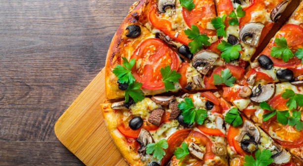 istock sliced Pizza with Mozzarella cheese, Tomatoes, pepper, olive, mushrooms, Spices and Fresh leaf. Italian pizza on wooden table background 1153486686