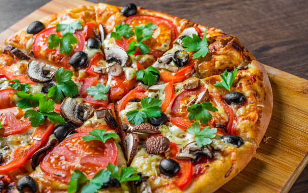 istock sliced Pizza with Mozzarella cheese, Tomatoes, pepper, olive, mushrooms, Spices and Fresh leaf. Italian pizza on wooden table background 1153486689