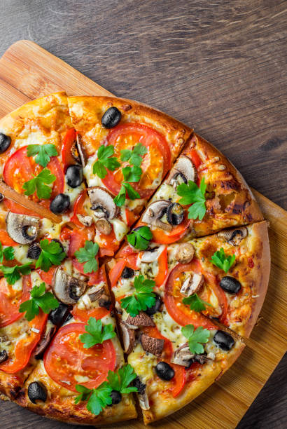 istock sliced Pizza with Mozzarella cheese, Tomatoes, pepper, olive, mushrooms, Spices and Fresh leaf. Italian pizza on wooden table background 1153486781