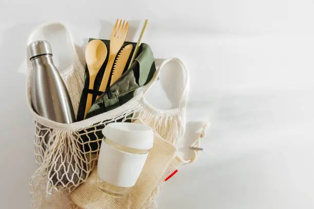Photo of Mesh market bag with bamboo cutlery, reusable coffee mug  and  water bottle. Sustainable lifestyle.  Plastic free concept.