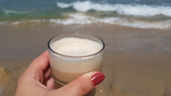 latte coffee in female hand against sea waters at background